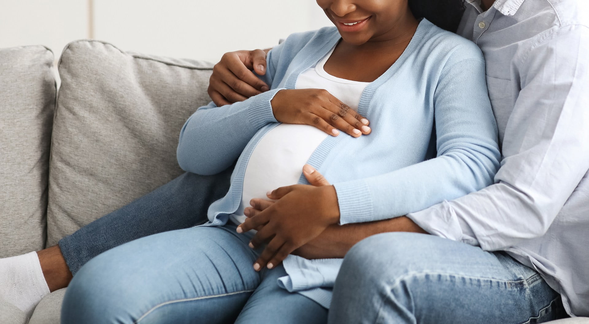 A pregnant woman and her husband cuddle on a couch. Weight loss surgery can affect fertility positively.