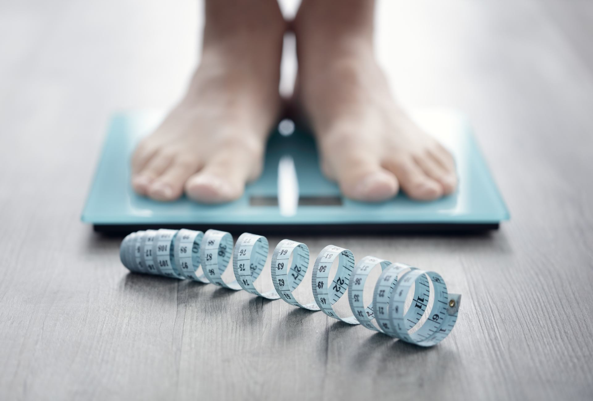 Closeup of a person’s feet on a scale with coiled measuring tape in foreground as they consider weight loss surgery. 