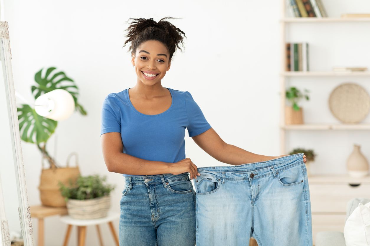 A female holding up a large pair of pants after weight loss surgery, illustrating that she’s lost weight.