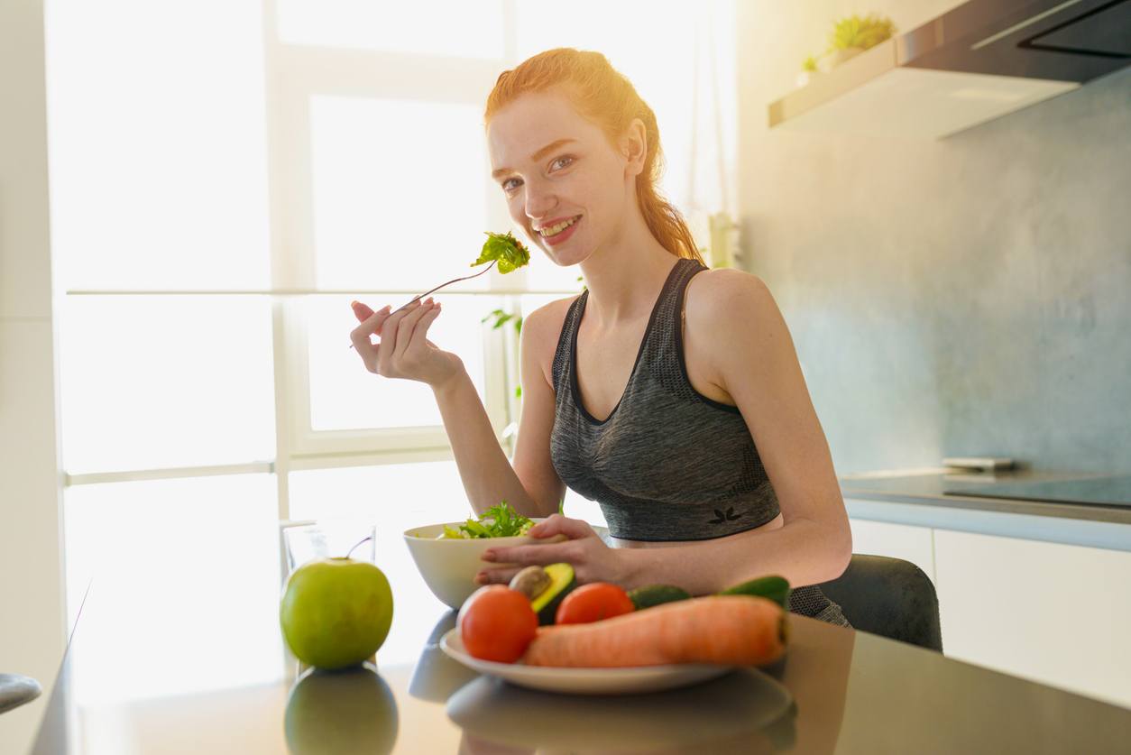 Athletic girl with gym clothes eats salad at a table