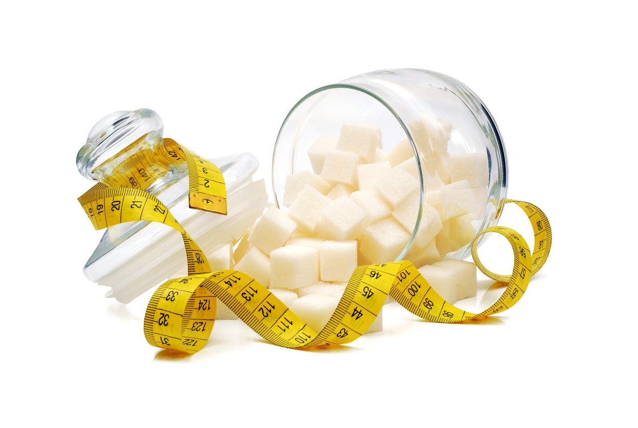 Sugar cubes spilled from the overturned glass sugar bowl and wrapped by tape measure