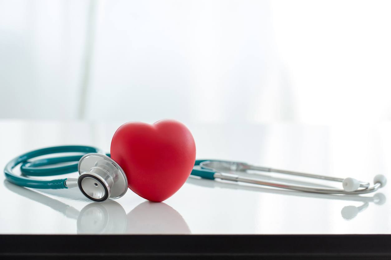 Red heart shaped hand exercise ball with doctor physician's stethoscope on white background.