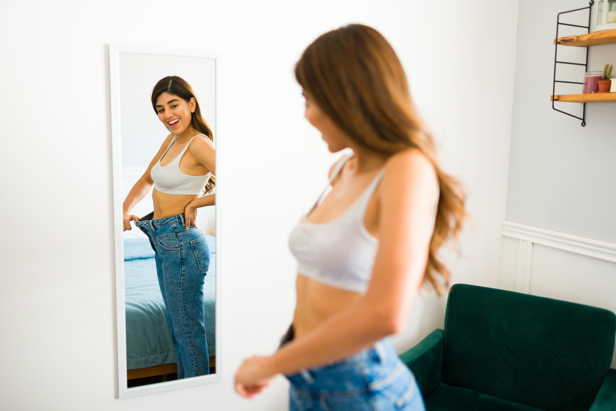 A girl in a gray top and bigger blue jeans illustrating weight loss.