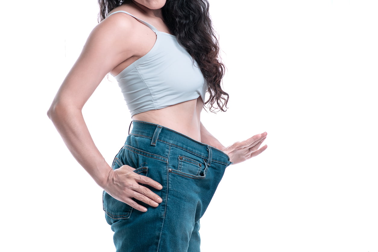 Woman measuring her jeans and stretching out her hand to illustrate noticing her weight loss.