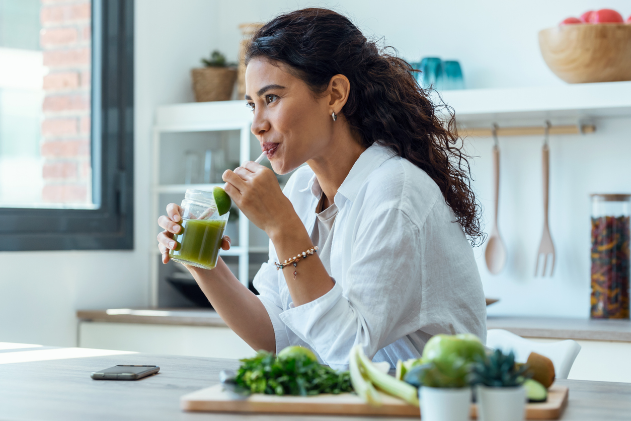 Woman looking sideways while drinking fruit detox juice in the kitchen at home.