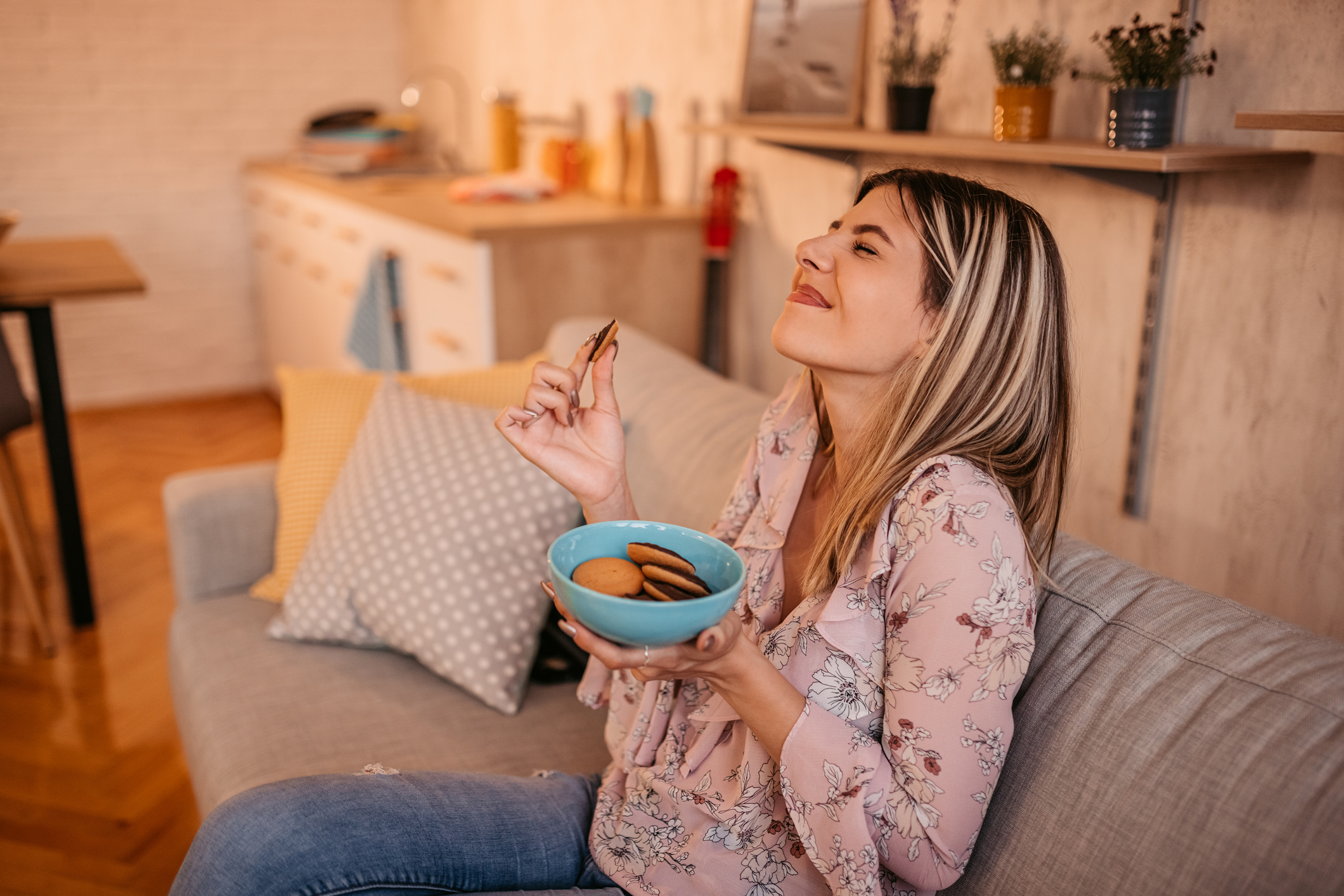 A woman enjoys a bowl of cookies while sitting on her couch. 