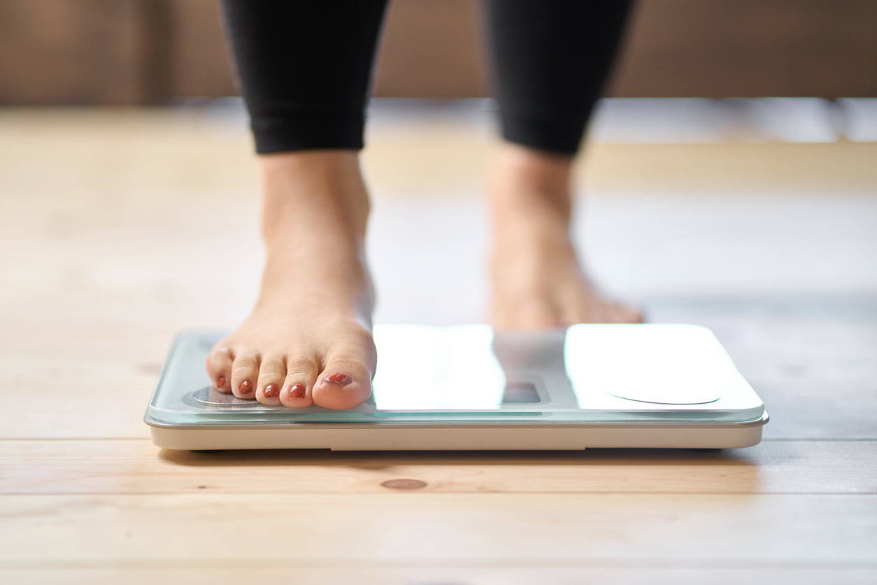 Person stepping on a scale to check their weight loss goals