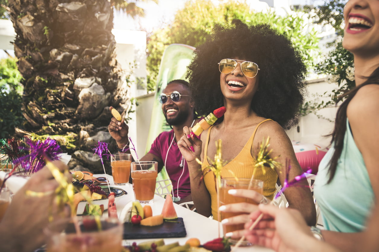 Happy individuals gather around a table outside to enjoy food and drinks